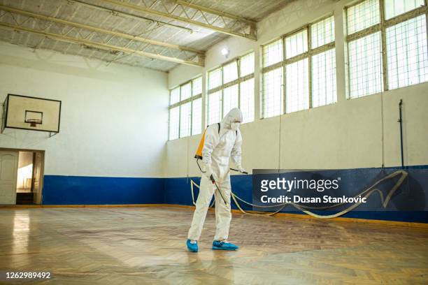 homme dans un costume de hazmat désinfectant la gymnastique d’école - décontamination photos et images de collection