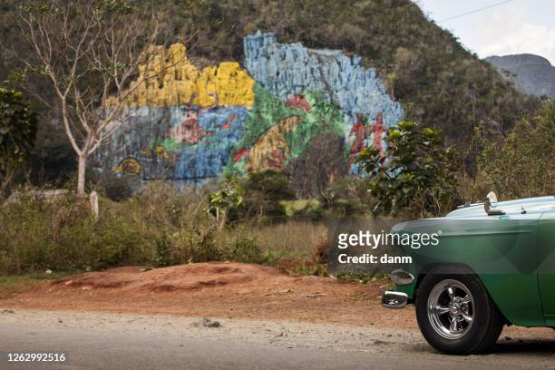 old american car with colourful mural wall from vinales, cuba - prehistoria stock pictures, royalty-free photos & images