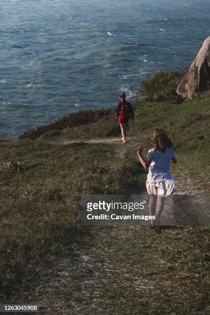 girl running in outdoor space on trail to the ocean with her mother - gravata stock-fotos und bilder
