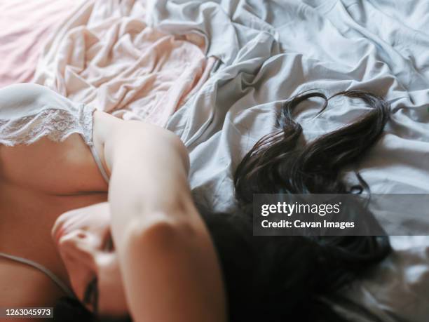 pensive brunette girl with hair forming a heart lying on the bed - vorspiel stock-fotos und bilder