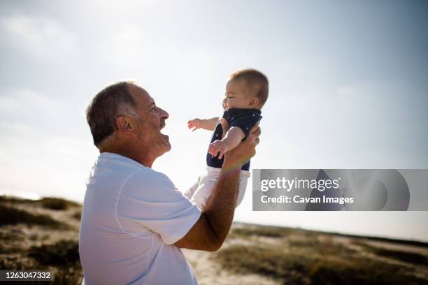 grandfather holding grandson while standing on beach - baby grandpa imagens e fotografias de stock