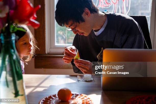 a father helps his child with a paper craft while she watches closely - looking closely stock pictures, royalty-free photos & images