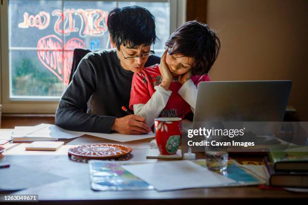 a father works home at the dining room table with his son in his lap - social projects address needs of struggling families stockfoto's en -beelden