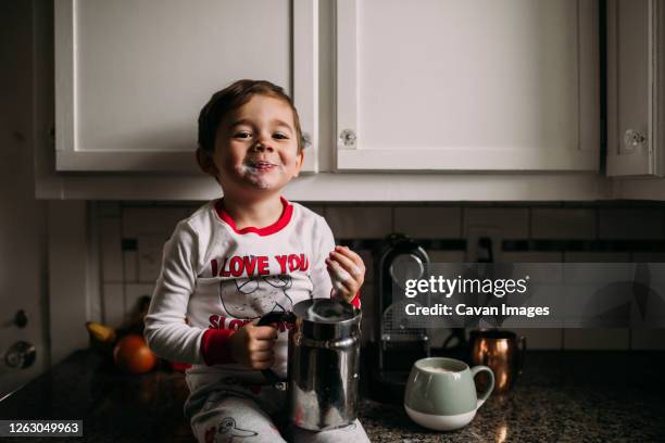 young boy sitting on kitchen counter with frothed milk on face - coffee capsules stock-fotos und bilder