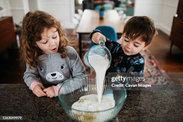 young brother and sister wearing pjs and making creakfast together - mixing stock pictures, royalty-free photos & images