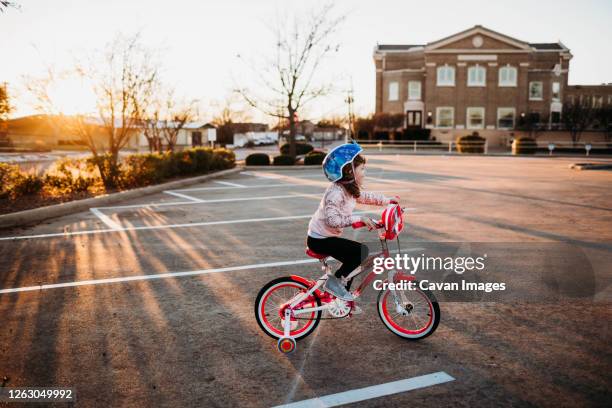 young girl riding a bike with training wheels in empty parking lot - training wheels stock pictures, royalty-free photos & images