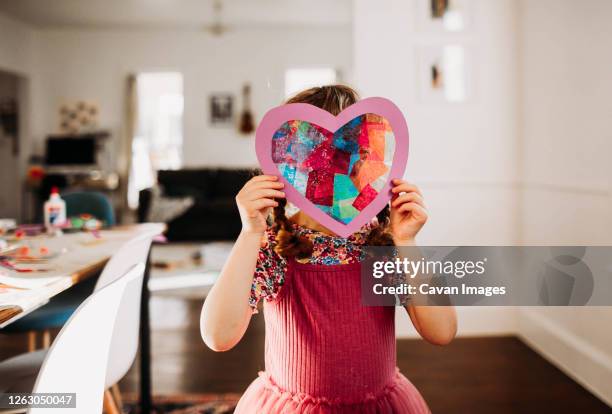 young girl standing inside with rainbow heart in hands - kunstnijverheid stockfoto's en -beelden