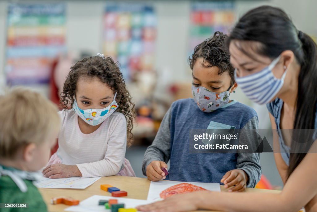 Grupo de niños coloreando mientras usa máscaras