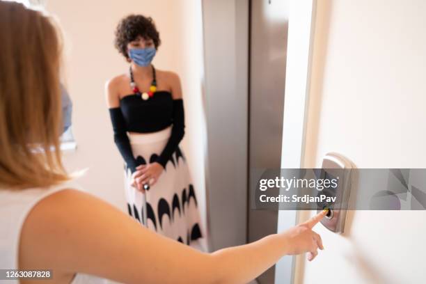 girls with protective face masks calling the elevator - social distancing elevator stock pictures, royalty-free photos & images