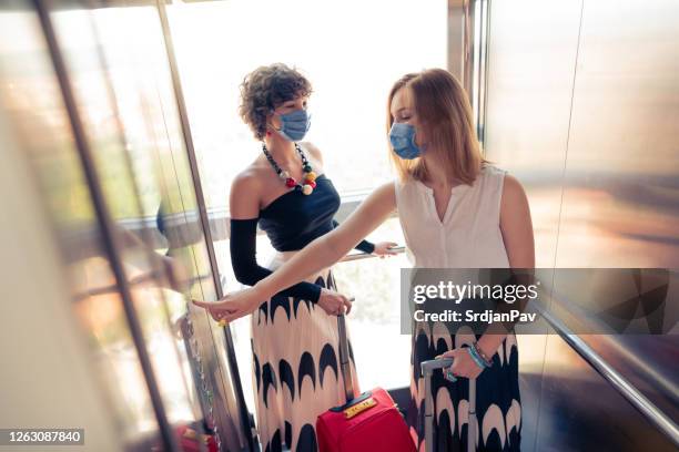 two young women riding an elevator with protective face masks - social distancing elevator stock pictures, royalty-free photos & images