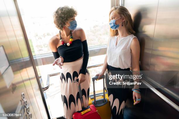 hotel guests riding an elevator with protective face masks and having a conversation - social distancing elevator stock pictures, royalty-free photos & images