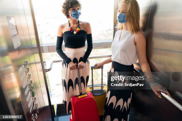 girlfriends with protective face masks riding a hotel elevator together - social distancing elevator stock pictures, royalty-free photos & images