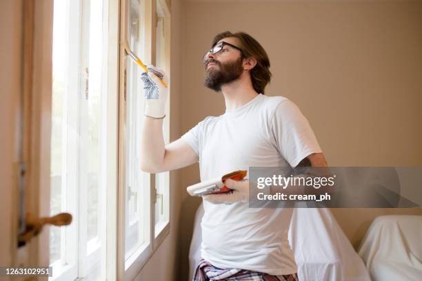 joven pintando marcos de ventanas en casa - marco de ventana fotografías e imágenes de stock