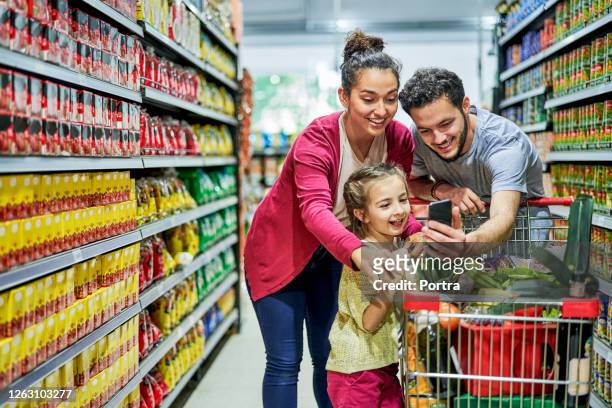 man showing phone family in supermarket - family shopping stock pictures, royalty-free photos & images