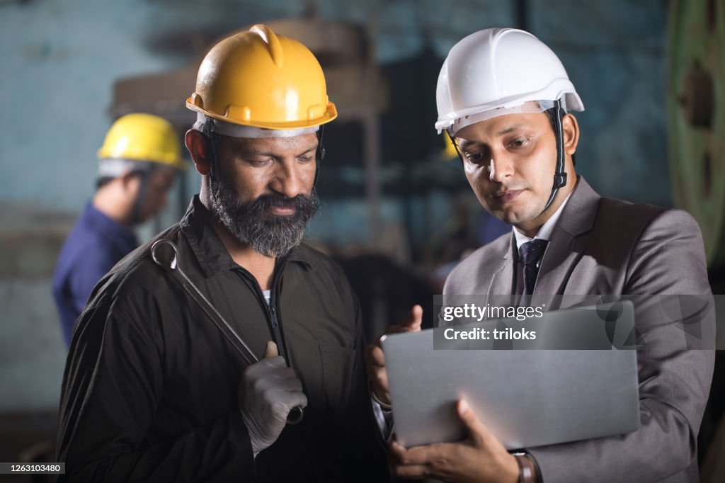 Mechanic with engineer using laptop and discussing at factory