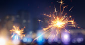 Happy New Year, Glittering burning sparkler against blurred city light background