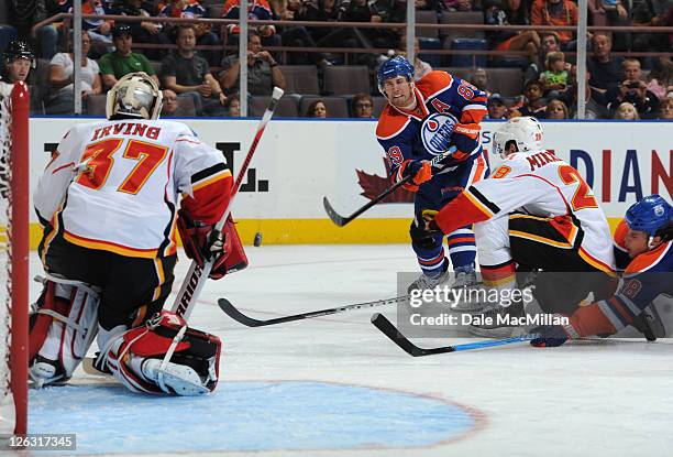 Sam Gagner of the Edmonton Oilers shoots the puck on Leland Irving of the Calgary Flames as teammate Brendan Mikkelson tries to block it during...