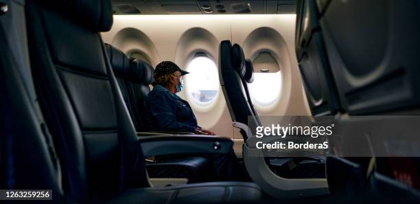 senior woman with protective mask looking the window on a plane after coronavirus pandemic - pandemic loneliness stock pictures, royalty-free photos & images