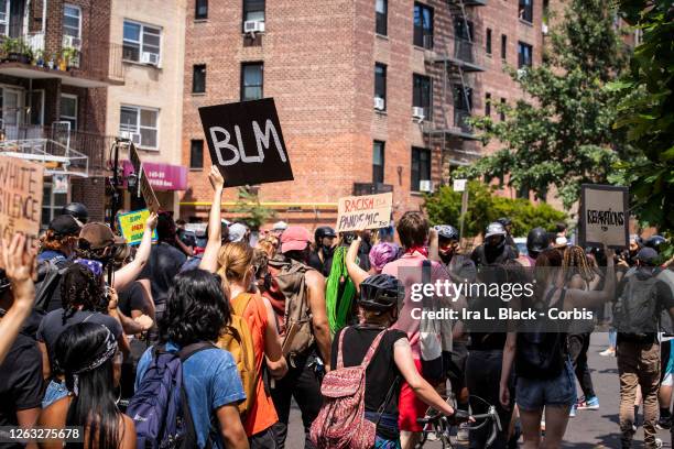 Large crowd of protesters wearing masks and carrying signs that say, "BLM" as they walk through neighborhoods at the Black Lives Matter protest in...