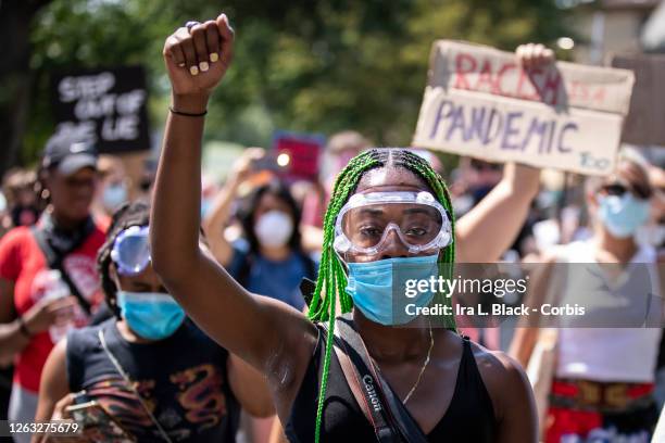 Protester wearing a mask and goggles in case of police conflict and pepper spray holds up a raised black power fist as they walk through...