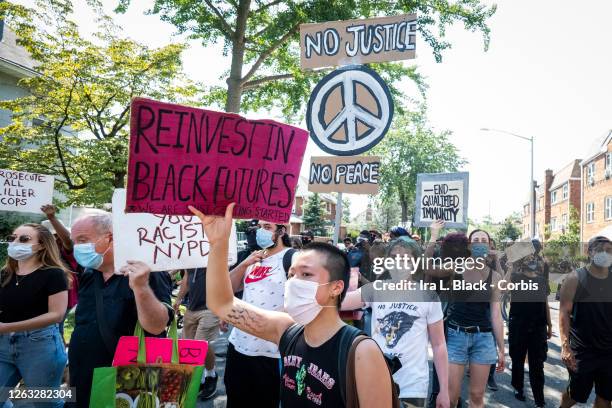 Protesters wearing masks and carrying signs that say, "Reinvest in Black Futures" and "No Justice No Peace" with a peace symbol as they walk through...