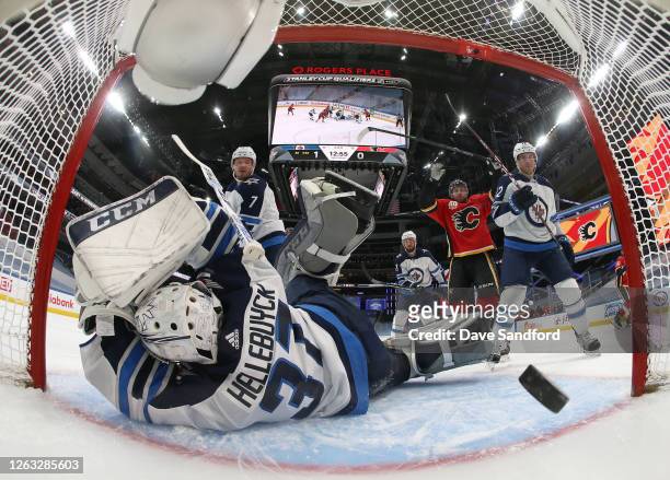 Goaltender Connor Hellebuyck of the Winnipeg Jets can't make the save on a shot by Johnny Gaudreau of the Calgary Flames for a goal as Elias Lindholm...