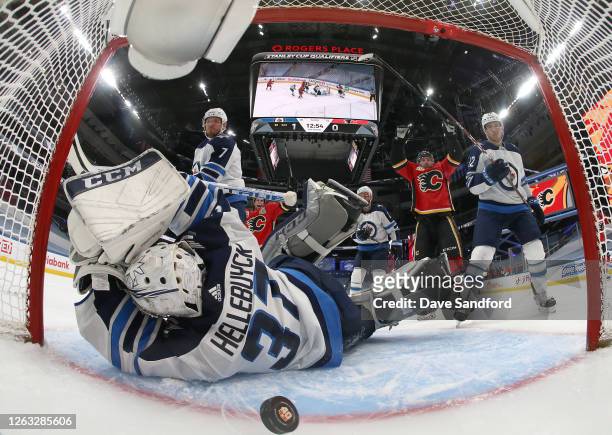Goaltender Connor Hellebuyck of the Winnipeg Jets can't make the save on a shot by Johnny Gaudreau of the Calgary Flames for a goal as Elias Lindholm...