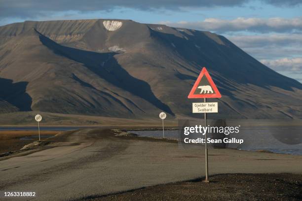 Mountains nearly devoid of snow stand behind a road and a polar bear warning sign during a summer heat wave on Svalbard archipelago on July 29, 2020...