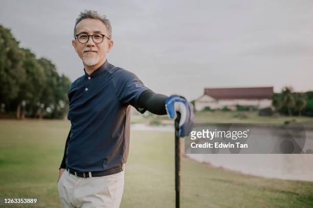 an asian chinese active senior man golfer standing with his golf club driver in the golf course after the golf game waiting and looking - golfer stock pictures, royalty-free photos & images