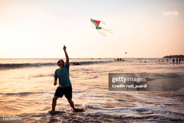 asian adult playing kite on the beach - indonesian kite stock pictures, royalty-free photos & images