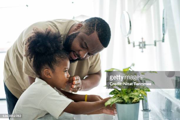side view of an african father helping his daughter wash her toothbrush and hands in the bathroom sink. - afro man washing stock pictures, royalty-free photos & images