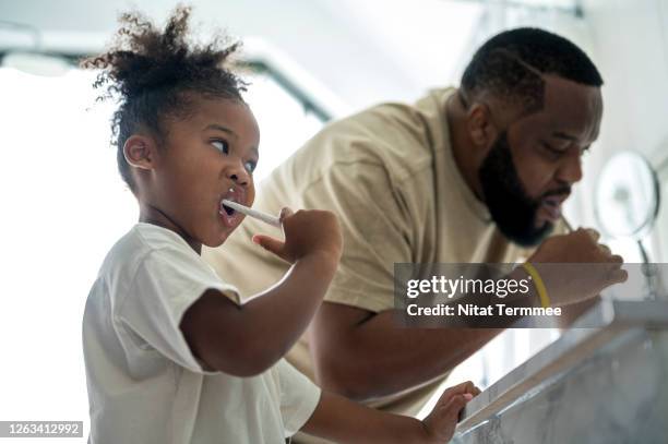 african adorable kindergarten age girls and father brushing teeth in bathroom at home. selective focus at a little girls missing a primary teeth. - dentista bambini foto e immagini stock