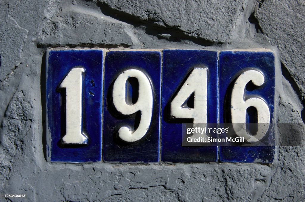 Number 1946 in blue and white ceramic tiles inland in a stone wall painted grey