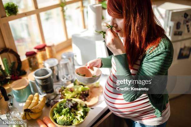 curious pregnant woman smelling fresh arugula while she making a salad in the kitchen - smelling food stock pictures, royalty-free photos & images