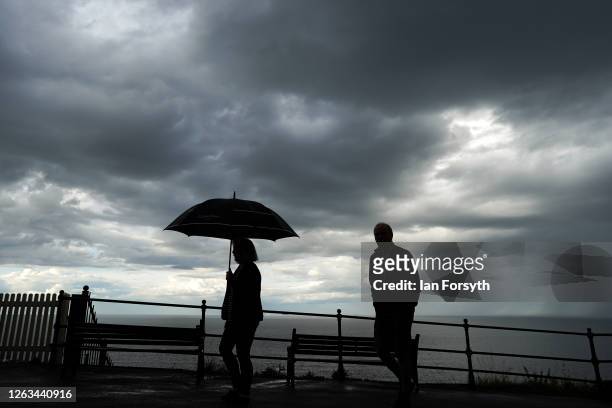 Couple walk along the upper promenade in Saltburn as thunder clouds pass overhead on August 02, 2020 in Saltburn By The Sea, England. Heavy showers...