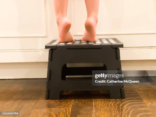 mixed-race toddler girl on a step stool stands on the tip of her toes at the kitchen sink - step stool imagens e fotografias de stock