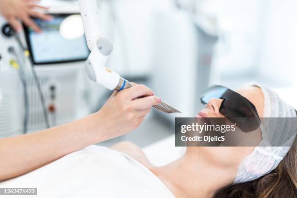 close-up of beautiful woman receiving laser procedures for her face. wearing protection glasses - laser face stock pictures, royalty-free photos & images