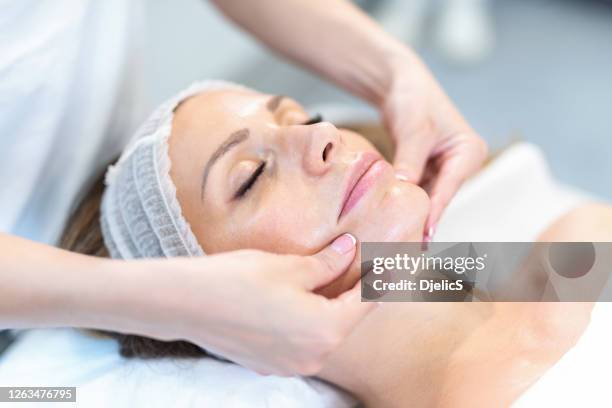 beautiful young woman receiving face massage. - clinic stock pictures, royalty-free photos & images