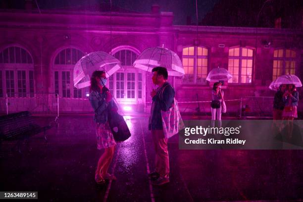 Visitors stand with umbrellas at the 'Purple Rain' installation at the Lycée Jacques-Decour on August 02, 2020 in Paris, France. Part of Festival...