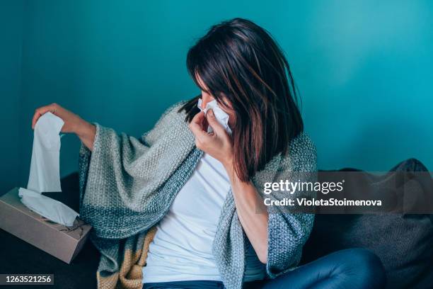 junge frau fühlt sich krank und bläst ihre nase mit einem gewebe zu hause. - papiertaschentuch stock-fotos und bilder