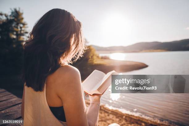 woman relaxes on lake pier, reads a book at sunrise - jetty stock pictures, royalty-free photos & images