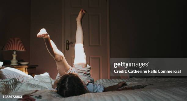 little girl lying on an old fashioned bed with her feet in the air - slumber party stock pictures, royalty-free photos & images