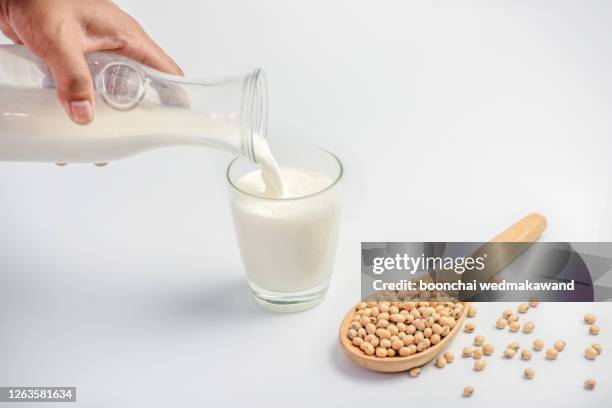 pouring soy milk into a glass and soy beans in a wooden spoon isolated on white background. - sojamilch stock-fotos und bilder
