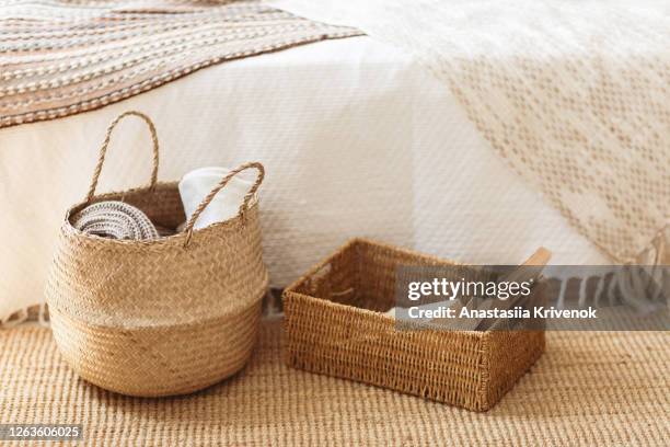 folded gray knitted plaid in straw basket on wicker carpet near bed. cozy hygge home style. fall winter season concept. close up, copy space. - mimbre fotografías e imágenes de stock