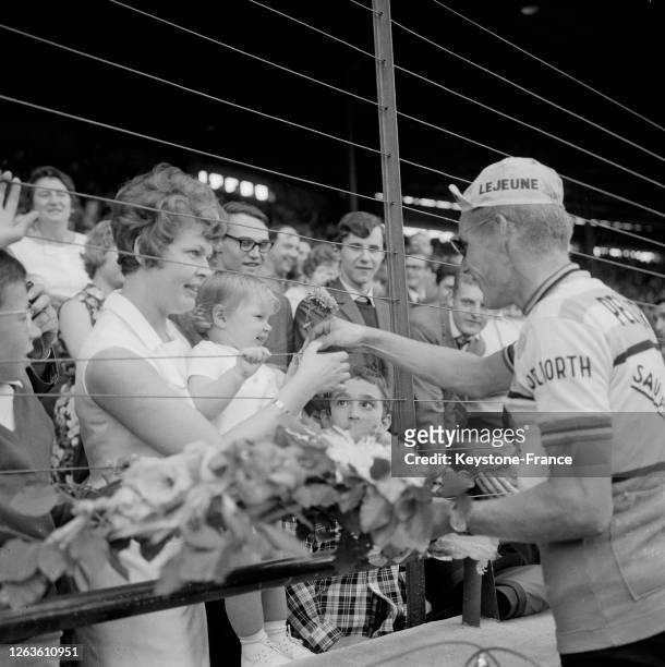 Jan Janssen, vainqueur du Tour de France 1966, remet une fleur de son bouquet à sa petite fille que tient sa femme dans les tribunes du vélodrome du...