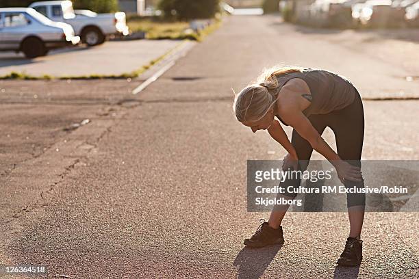 runner resting on suburban street - runner tired stock pictures, royalty-free photos & images