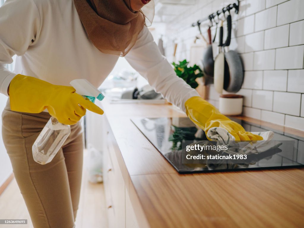 Moslim meisje dat kooktop het koken paneel op keuken schoonmaakt.