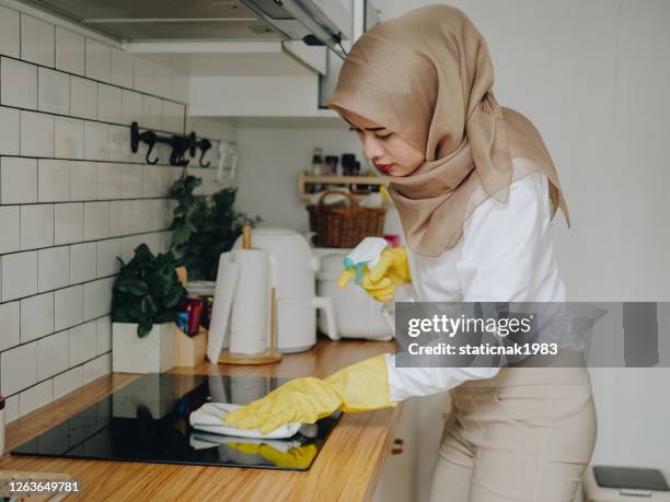 jonge moslimvrouw die haar bovenkant van het keukentellerblad thuis schoonmaakt - burner stove top stockfoto's en -beelden