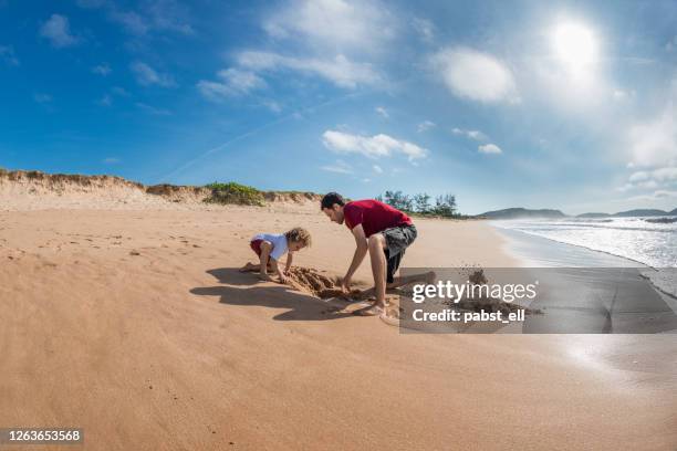 père avec le trou de creusement de fils sur la plage, búzios - creuser photos et images de collection