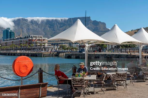 Cape Town, South Africa, Landscape view of the waterfront with tourists eating and drinking and cloud creeping over the summit of Table Mountain.